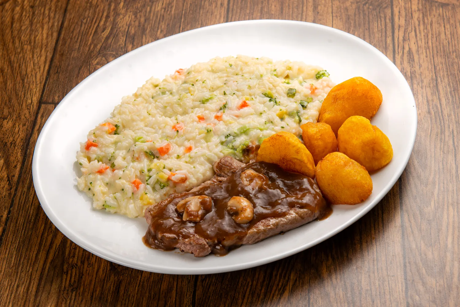 Escalope nobre de mignon ao molho madeira acompanhado de risoto de legumes e batatas douradas, em prato branco sobre madeira rústica