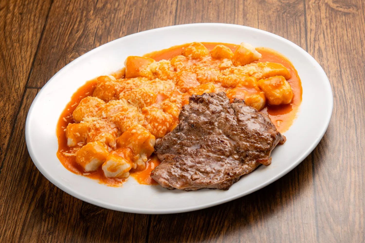 Filé mignon grelhado com nhoque gratinado ao molho madeira, servido em prato branco sobre mesa de madeira rústica